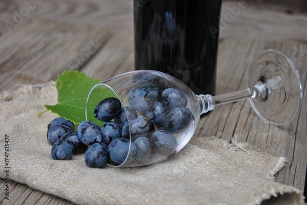 Fototapeta juicy grapes in an overturned glass glass on a wooden table with burlap. wine making concept