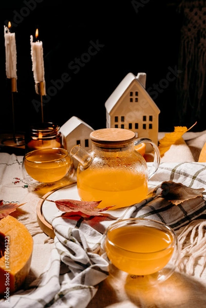 Fototapeta Warm autumn composition with glass teapot of steaming pumpkin tea, candles and fall decor. Cozy lifestyle concept.