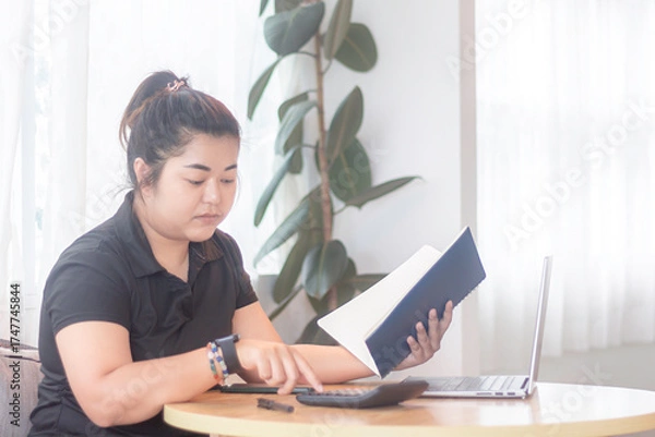 Obraz Young woman studying at a table with a laptop and calculator in a bright, modern space