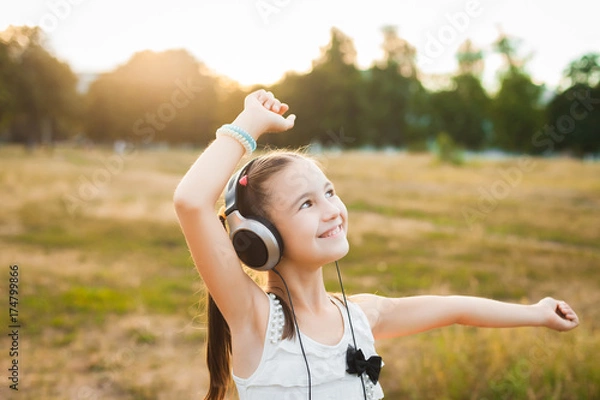 Obraz joyful girl listening music and dancing in the field