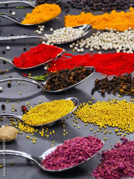 Fototapeta Colorful spices arranged in spoons on a black surface showcasing culinary variety and texture