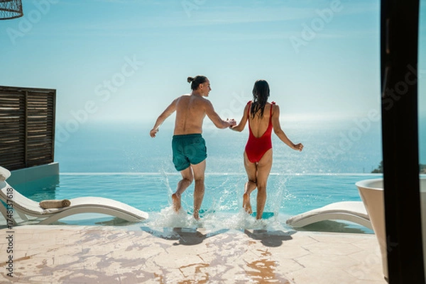 Fototapeta A joyful couple jumping into a swimming pool during their summer holiday.