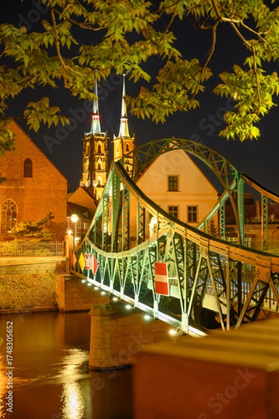 Fototapeta Vertical photo showing illuminated bridge and reflections on the river near Ostrów Tumski in Wroclaw, Poland. Peaceful evening atmosphere ideal for travel blogs, posters, and architecture visuals.