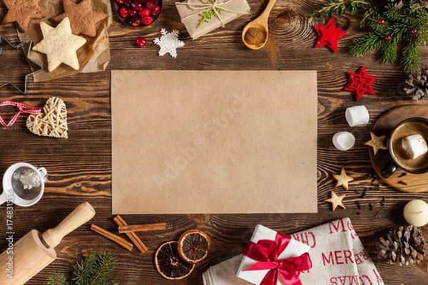 Fototapeta Christmass decorations baking in the form of stars, candle, and empty piece of paper on center. Christmass background with cup of coffee, gift with red ribbon on wooden background.