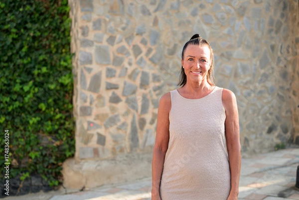 Obraz Portrait of a happy mature tourist woman standing in front of a stone wall in Spain