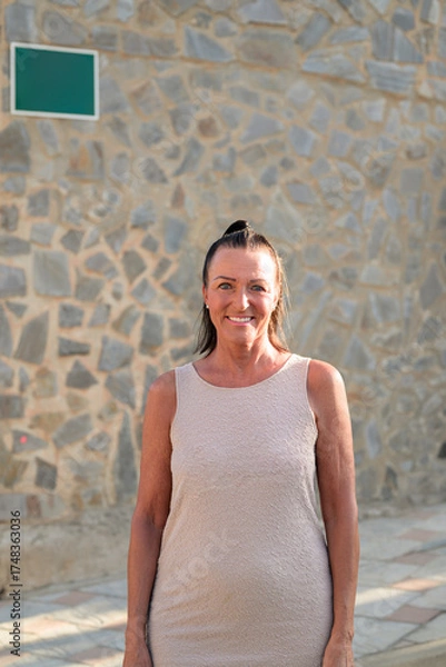 Obraz Portrait of a happy mature tourist woman standing in front of a stone wall in Spain