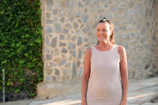 Obraz Portrait of a happy mature tourist woman standing in front of a stone wall in Spain
