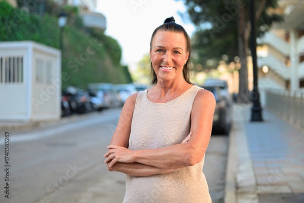 Obraz Portrait of a beautiful mature Scandinavian woman smiling with arms crossed in the street