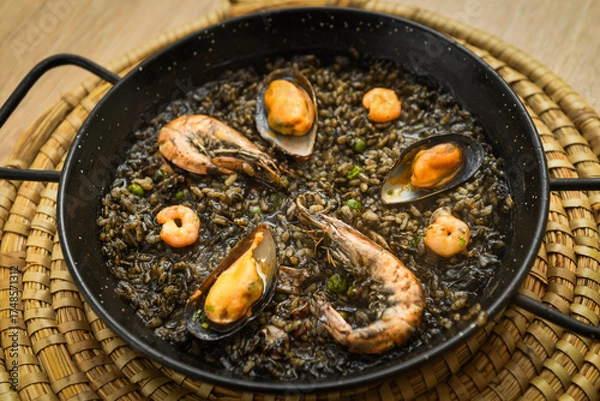 Fototapeta Paella with black rice, mussels and shrimps in a pan