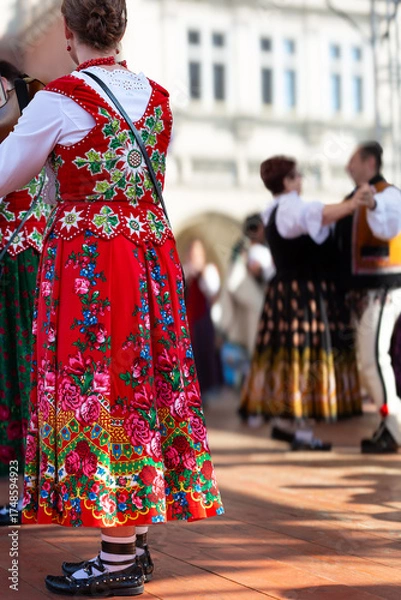 Fototapeta Woman in traditional for Polish highlanders of Tatra mountains region on a stage during cultural event, in the background other dancers in soft focus
