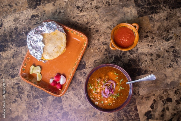 Fototapeta Birria stew with red onions and cilantro served next to a taco, salsa, lime, and radish