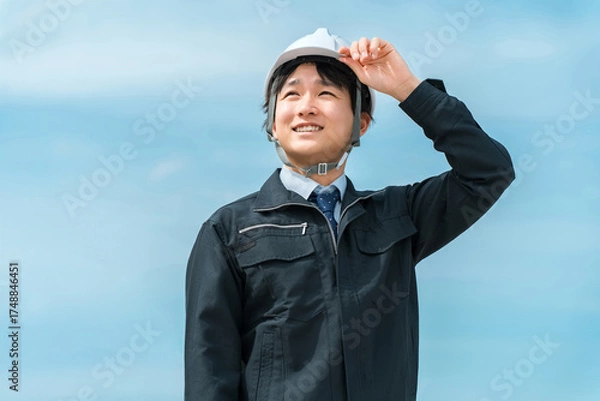 Obraz 青空の下にいる作業着姿のヘルメットを被った男性
