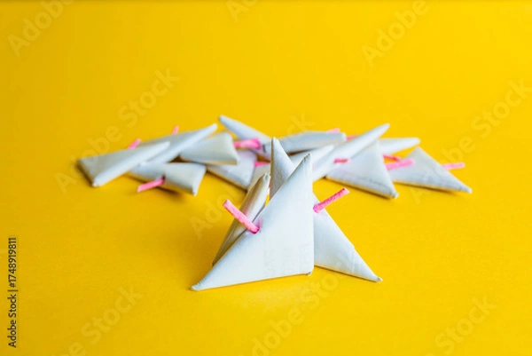 Fototapeta Low-angle shot of a group of white paper triangular-shaped firecrackers, with prominent pink fuses against a vibrant yellow background.