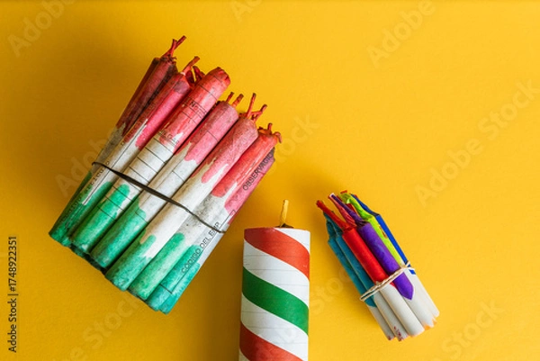 Obraz Top view of two bundles of firecrackers tied with rubber bands and a large striped explosive on a bright yellow background.