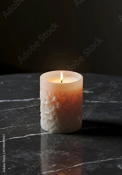 Fototapeta A decorative, beige candle with textured design sits on a dark gray marble surface. Burning candle with intricate design against a dark background.