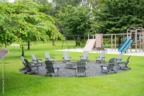 Fototapeta a group of gray Adirondack chairs circled around on a bonfire pit outside on a well maintained lawn 