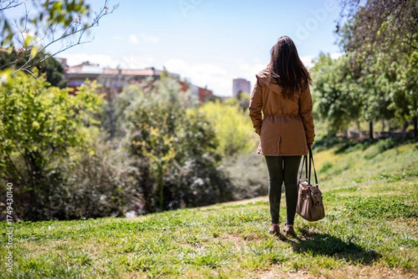 Obraz Brunette woman enjoying a peaceful moment in nature, wearing a stylish jacket and bag, taking in the beauty of the outdoor scenery in bright sunlight