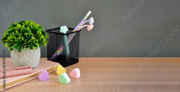 Fototapeta On the wooden tabletop lies a notepad with a marker and erasers, a pen stand, and a flower.