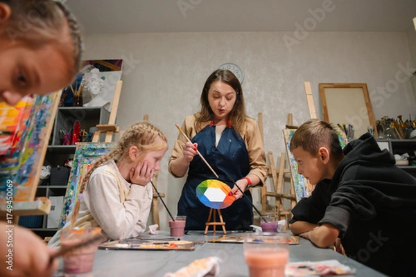 Fototapeta Artist explains how to mix and combine colors. Teacher learn children to draw pictures in an art lesson. Childs painting in workshop. Kids drawing brush on easel. Education, learning concept.