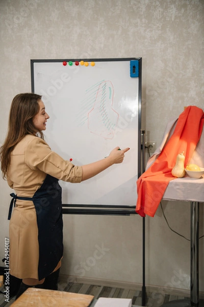 Fototapeta Education and learning concept. Female is drawing a picture in art class. Woman painting in a workshop. Girl mixing and combining colors. Art lesson. People drawing with brush on easel.