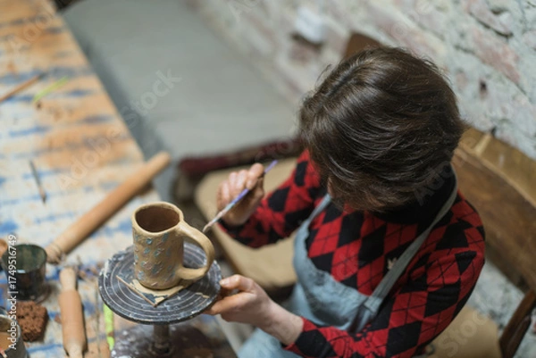 Fototapeta Girl paints her own handmade clay mug. Pottery teaching lesson. Potter makes dishes from clay, ceramics. Top view.