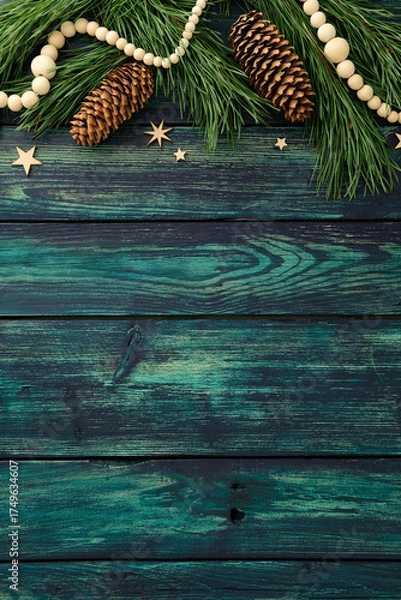 Fototapeta Rustic teal wood background with pine branches, cones, wooden beads and stars. Cozy Christmas flat lay for festive design, greeting card or seasonal decoration.