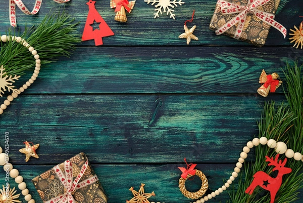 Fototapeta Christmas flat lay with gift box, wooden ornaments, pine branches and festive decor on rustic teal background, perfect for holiday greeting or seasonal design.