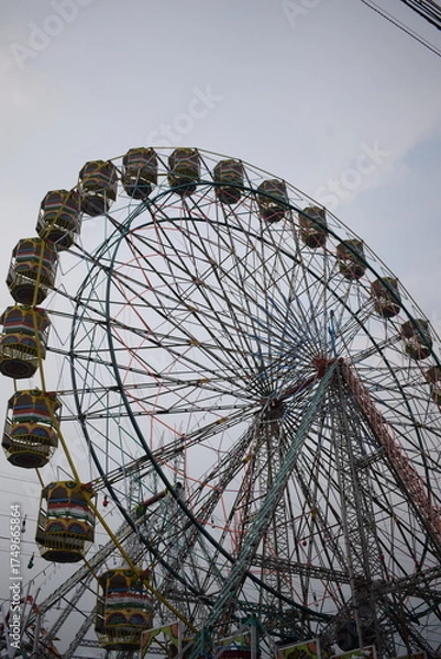 Fototapeta Closeup of multi-coloured Giant Wheel during Dussehra Mela in Delhi, India. Bottom view of Giant Wheel swing. Ferris wheel with colourful cabins during evening time.