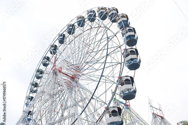 Fototapeta Closeup of multi-coloured Giant Wheel during Dussehra Mela in Delhi, India. Bottom view of Giant Wheel swing. Ferris wheel with colourful cabins during evening time.