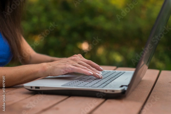 Fototapeta Close-up view of female hands on laptop keyboard. Student learning outdoors.