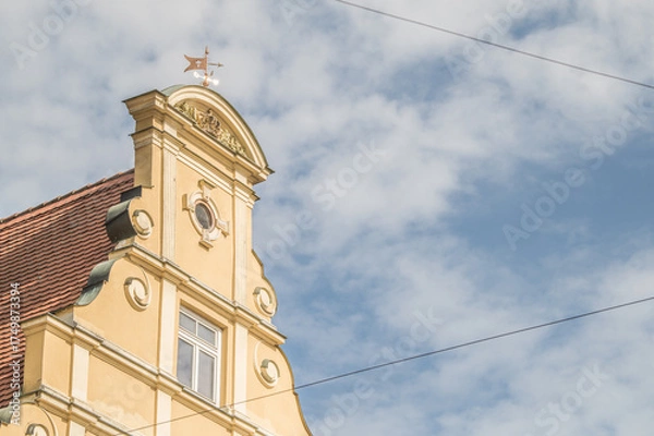 Fototapeta Giebelständiger Satteldachbau mit Neurenaissancefassade mit Sprossenfenstern und Wetterfahne am Weinmarkt in Nördlingen vor blauem Himmel mit Wolken