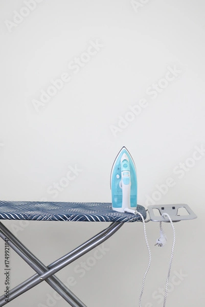 Fototapeta A modern iron standing on an ironing board against a plain white wall. Minimalist home interior concept with copy space. Clean, simple, and domestic lifestyle background. High quality photo