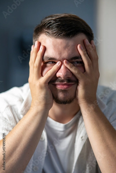 Fototapeta jeune homme se cachant le visage avec ses mains avec les yeux visibles avec le sourire
