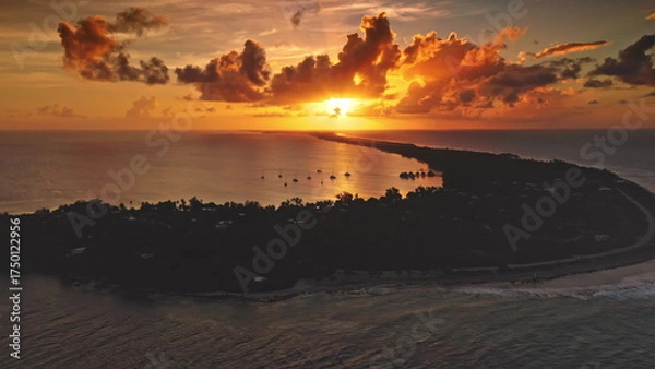Fototapeta Fakarava Atoll: bright sunset illuminate South Pacific Ocean with sailboats inside the island lagoon silhouette and dramatic orange clouds during golden hour in French Polynesia. Aerial drone