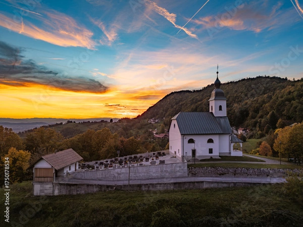 Fototapeta A stunning aerial view of the Church of Holy Cross (Sveti Križ) in Križevska vas above Dolsko pri Ljubljani at sunset, surrounded by lush greenery and rolling hills.