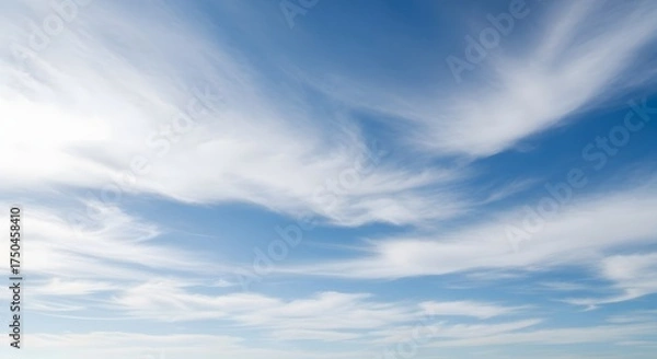 Obraz Wispy white cirrus clouds drift across a bright blue summer sky on a clear day.