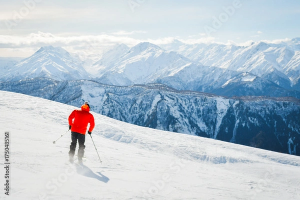 Fototapeta Male adult skier in red jacket go freestyle off piste carving turns to fresh powder mountainside in snowy mountain resort during sunny winter day adventure in alpine high mountains