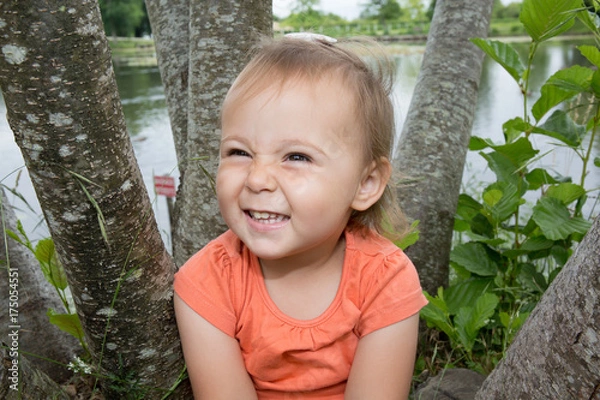 Fototapeta Portrait of a smiling little girl on green grass park and lake