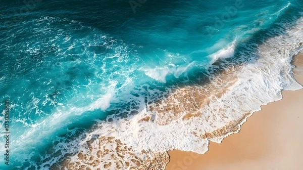 Fototapeta Turquoise ocean waves crash onto a sandy beach from above.