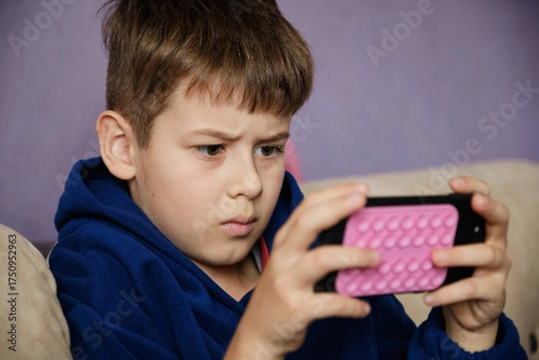 Fototapeta Young boy engrossed in watching a video or playing a game on a smartphone.
