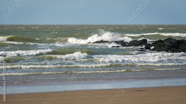 Fototapeta Storm build big waves, they break on the stone wall at the beach, stormy waves shine in the evening light, North Sea beach before sunset with waves of the ocean