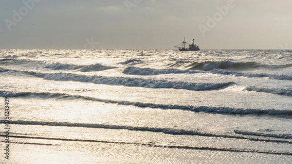 Fototapeta single ship is sailing on the North Sea, ship, sails and waves shine in the evening light, North Sea beach before sunset with waves of the ocean