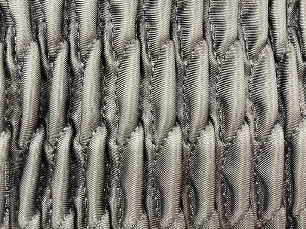 Obraz Close-up of gray quilted fabric texture with a geometric pattern. Detailed textile surface showing soft padded stitches and shiny synthetic material, background for fashion or upholstery design.
