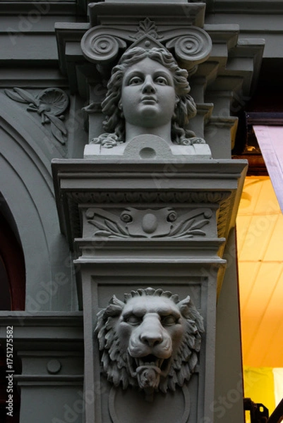Fototapeta closeup of a facade with a lions head, a womans head on a column and a bit of an arch