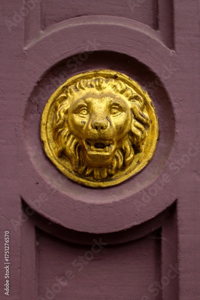 Fototapeta closeup of a lions head golden relief, on an old red colored stone building 
