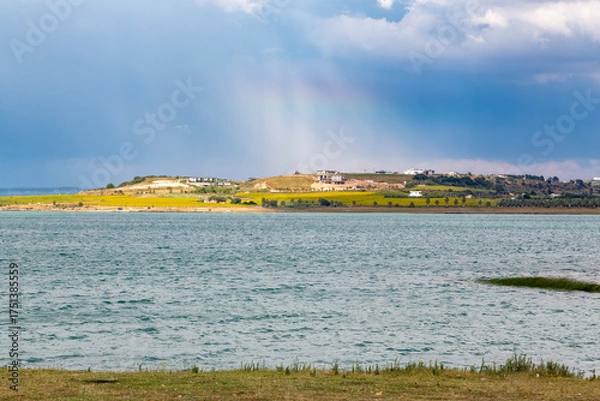 Fototapeta A peaceful lakeside scene. Clouds carry rain. Sunlight shines through the clouds onto the hills opposite.