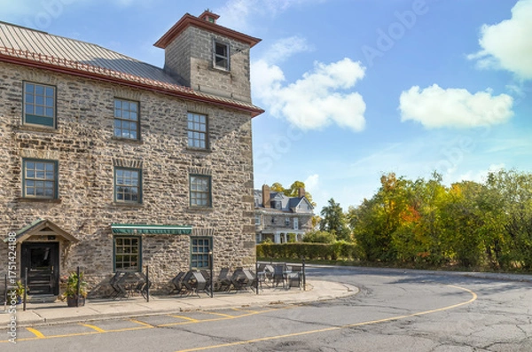 Fototapeta Exterior daytime view of century-old three storey limestone building with tower, paned windows and doors, old house in background, nobody