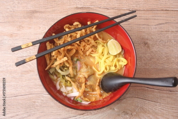 Fototapeta Northern Thai curry noodle soup with chicken (Khao Soi), a popular dish, served in a red bowl with chopsticks and spoon.