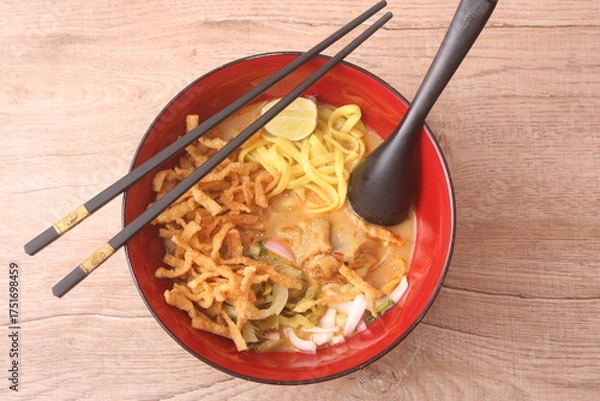 Fototapeta Northern Thai curry noodle soup with chicken (Khao Soi), a popular dish, served in a red bowl with chopsticks and spoon.