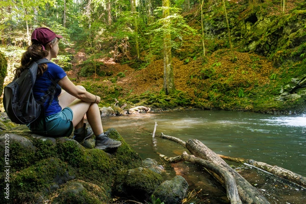Fototapeta A tourist sitting by a river in the forest in Besse-et-Saint-Anastaise, Auvergne